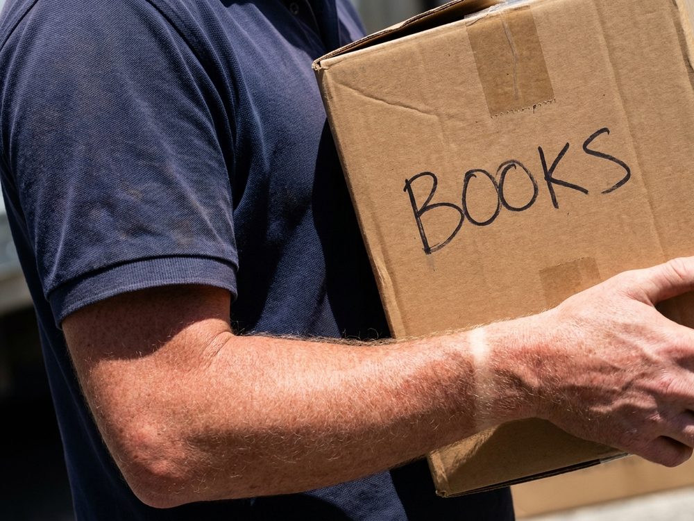 A removalist carrying a carton against his side.
