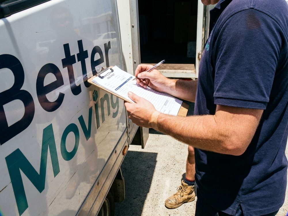 A removalist writing on a clipboard braced against the side of the truck.